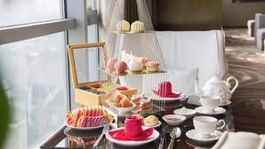Una mesa servida con servicio de té y pastelería, un soporte escalonado con postres, y vistas al exterior a través de una ventana.