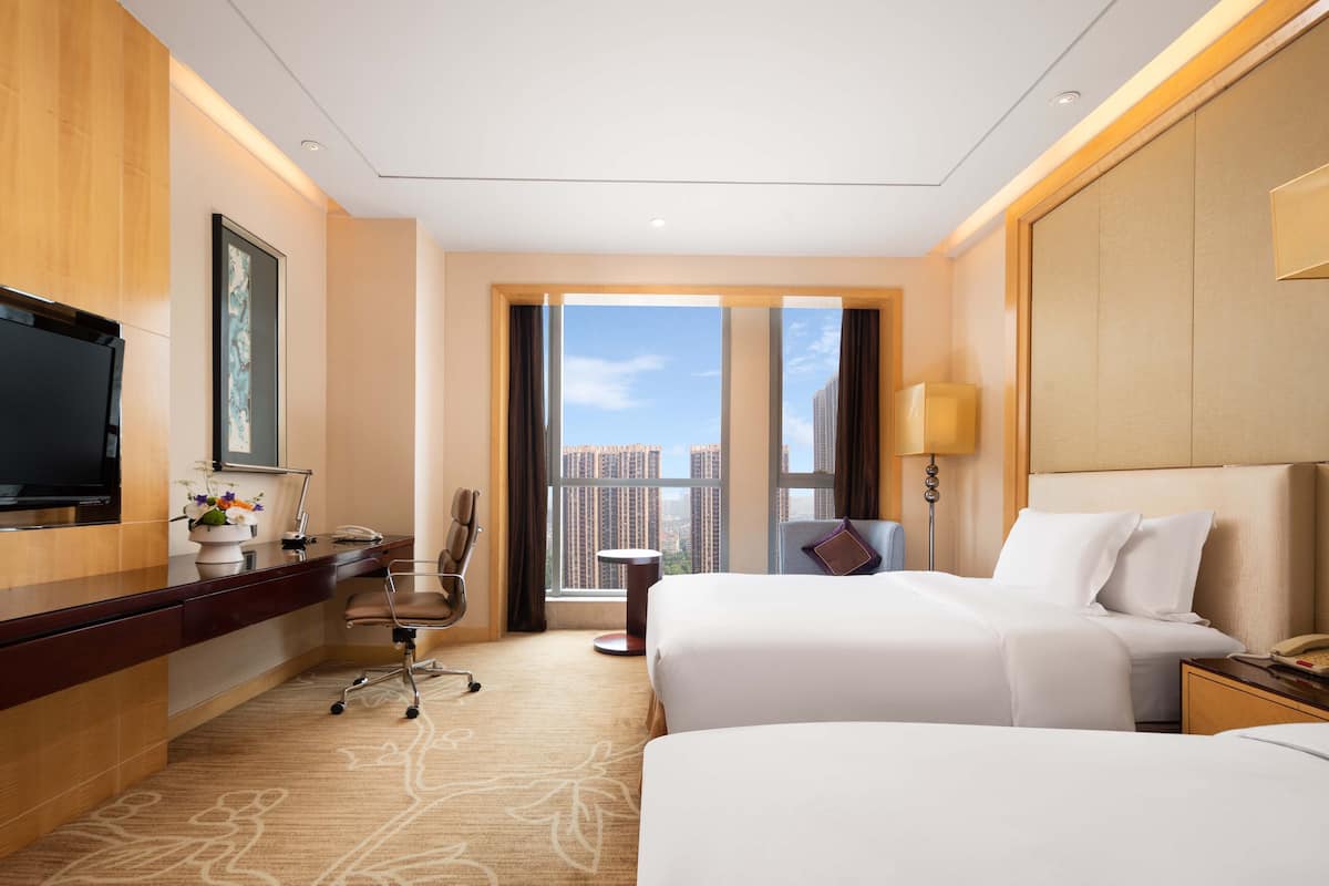 A hotel room with a large bed, a desk with a computer, a chair, a TV, and a view of the city.