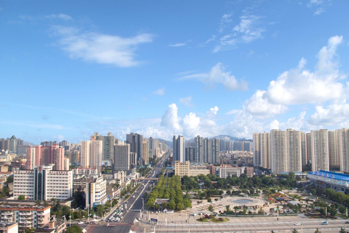 A cityscape with high-rise buildings, a central roundabout, and a clear blue sky.