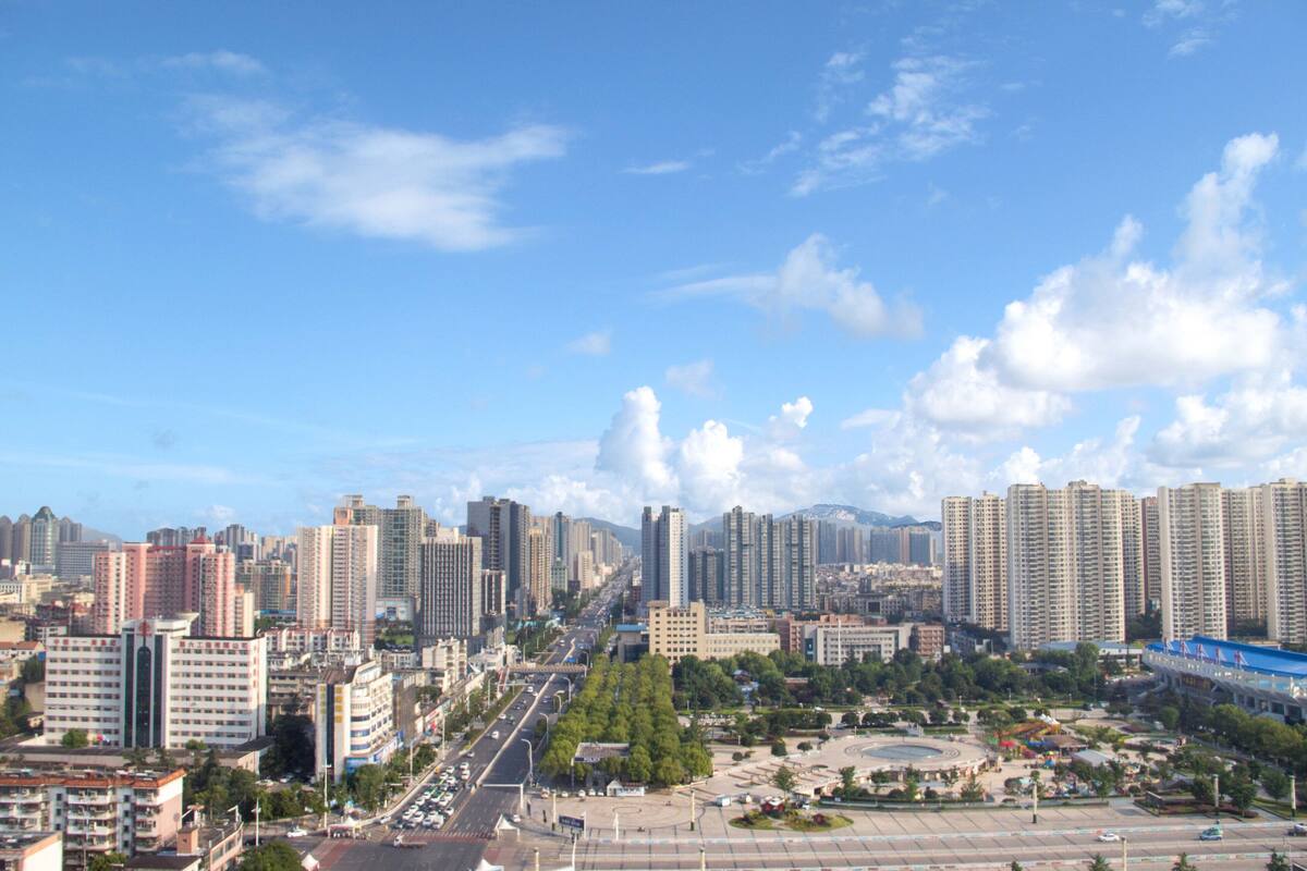 A cityscape with high-rise buildings, a central roundabout, and a clear blue sky.