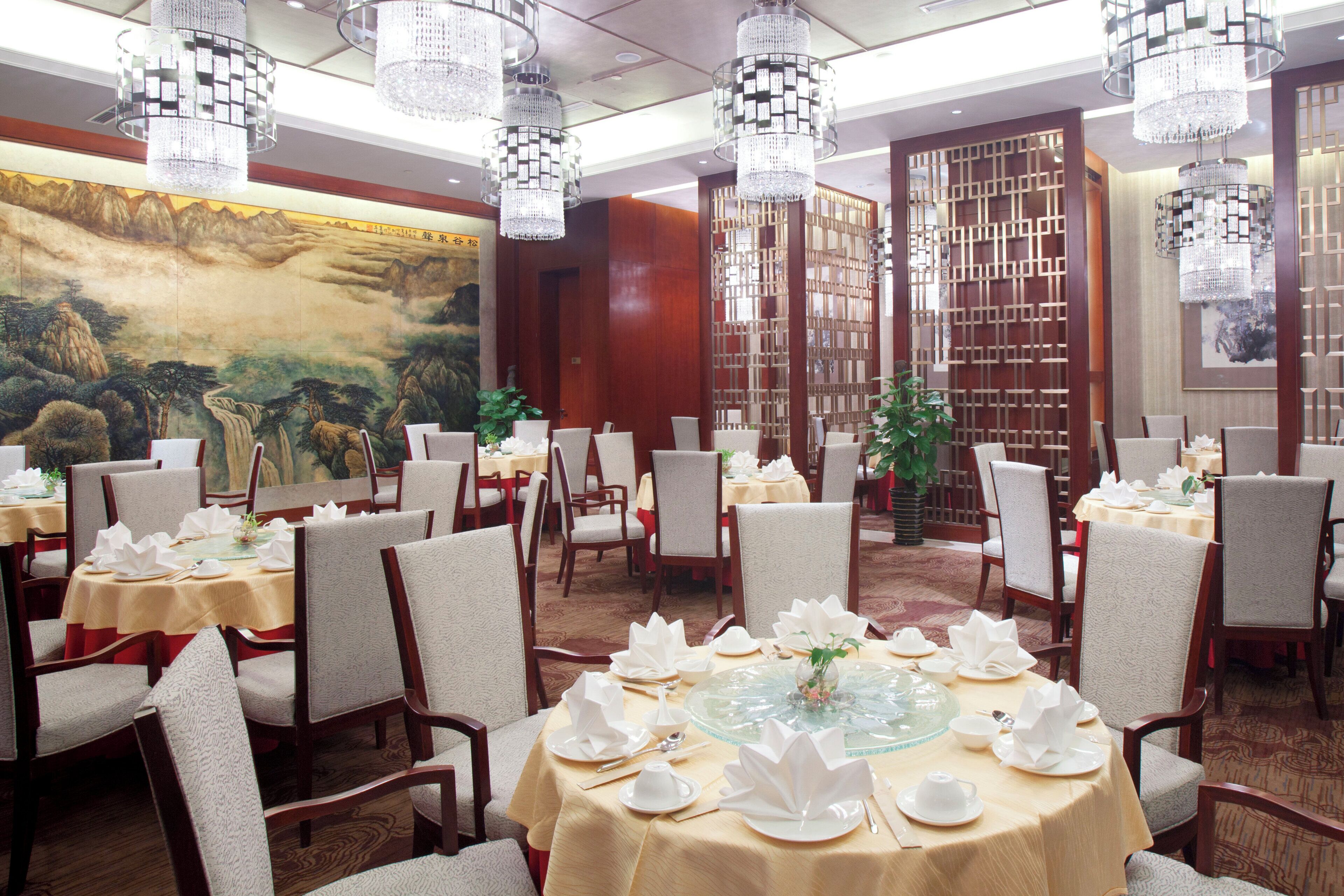 Un restaurante con mesas redondas dispuestas para comer, con una pintura tradicional china de paisaje en la pared.