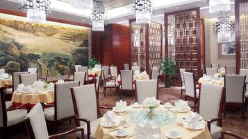 Un restaurante con mesas redondas dispuestas para comer, con una pintura tradicional china de paisaje en la pared.