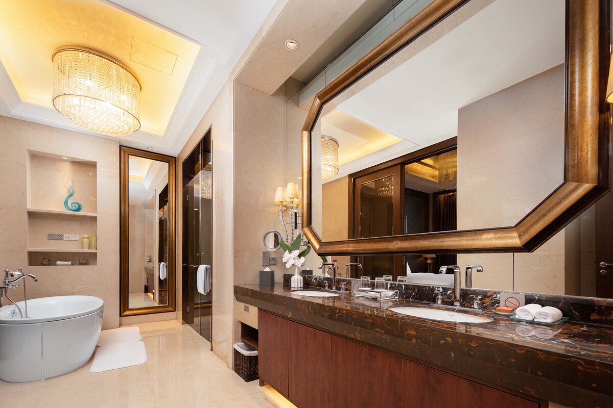 A modern bathroom with a large mirror, two sinks, a bathtub, and a vanity with a marble countertop.