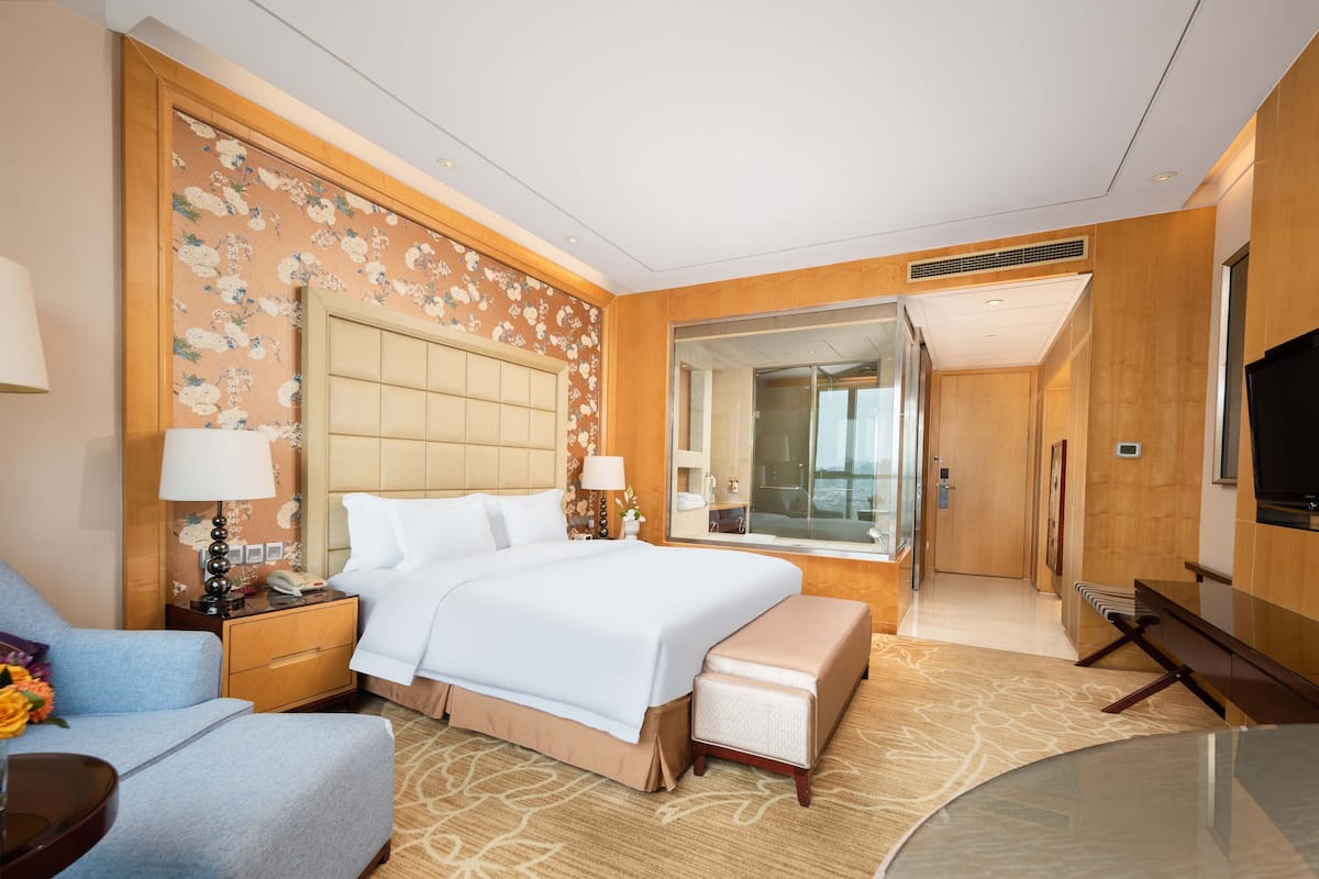 A hotel room with a large bed, a seating area, a desk, and a television.