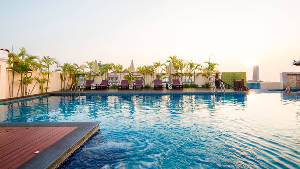 A pool area with lounge chairs and palm trees. - Aiyara Palace (Pattaya)