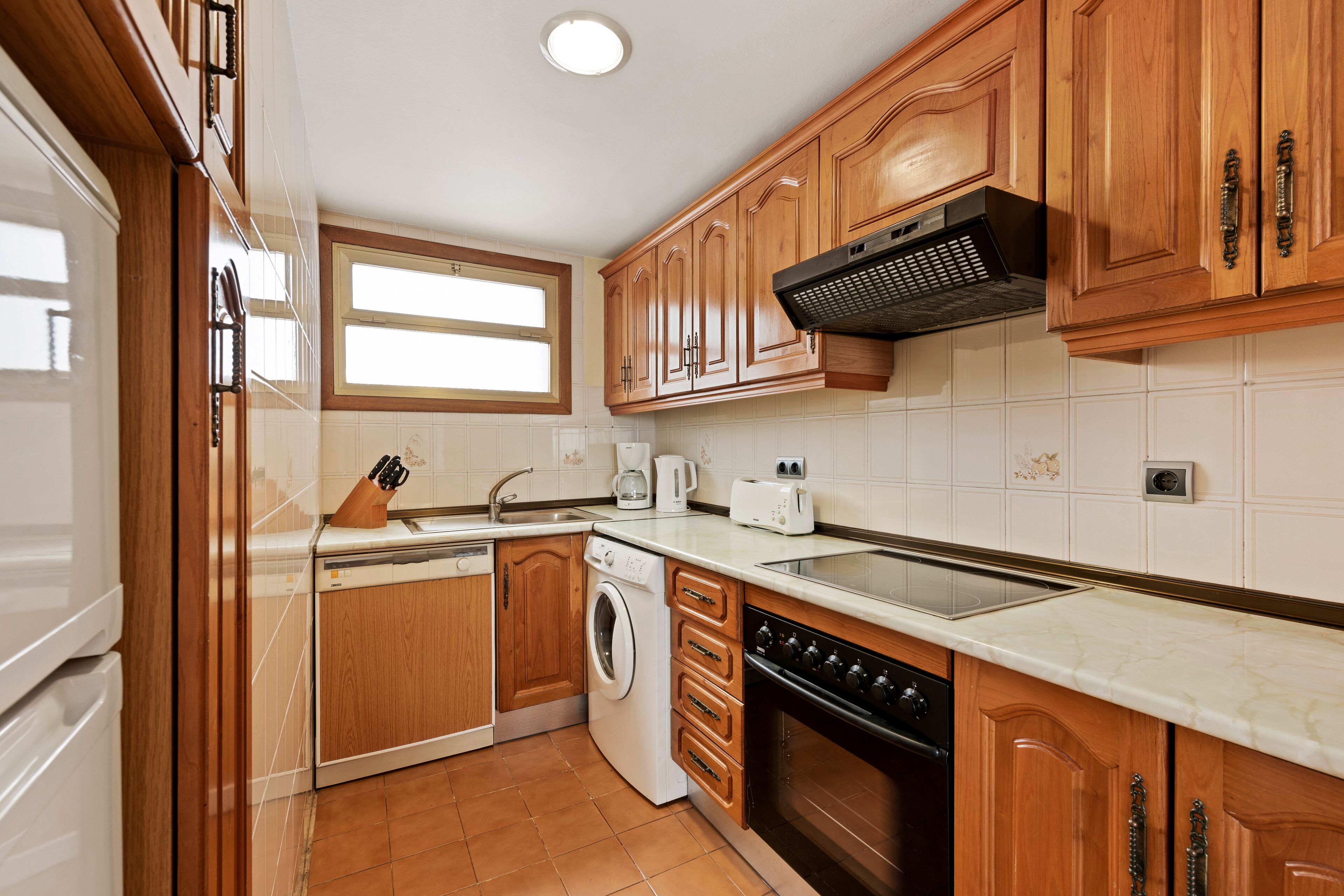 Une cuisine avec des meubles de rangement en bois, un lave-linge, un lave-vaisselle et une cuisinière.