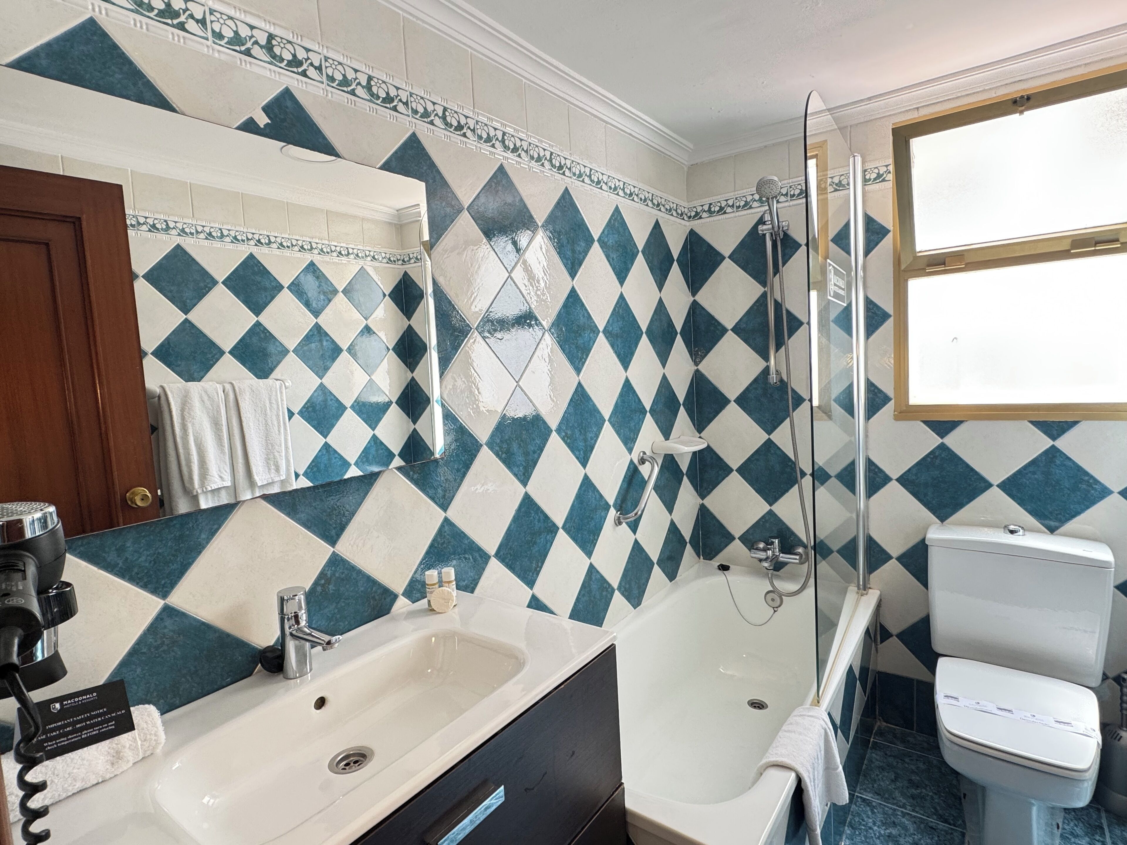 A bathroom with a sink, bathtub, and toilet, featuring blue and white diamond-patterned tiles.