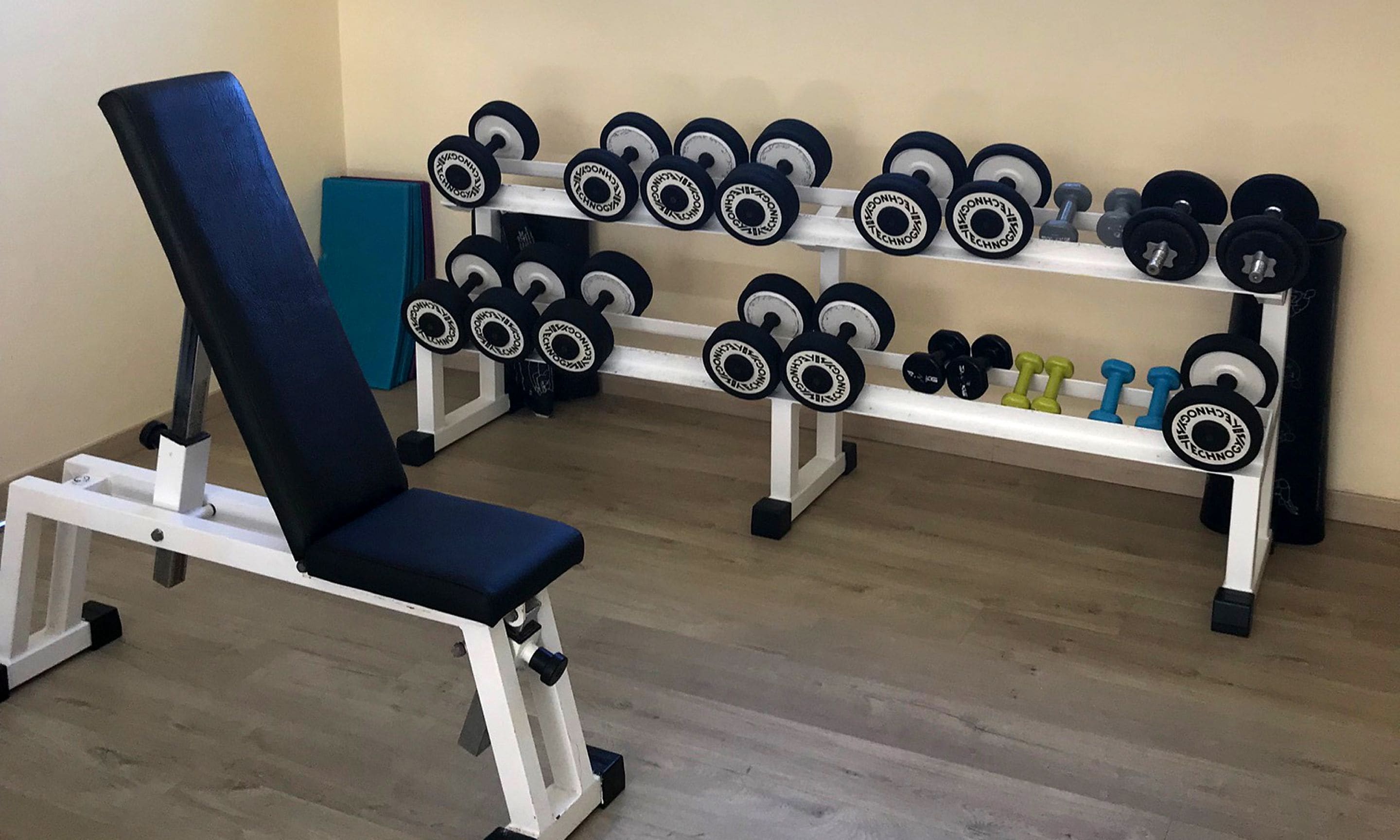 A gym with a bench press, a rack of dumbbells, and a yoga mat.