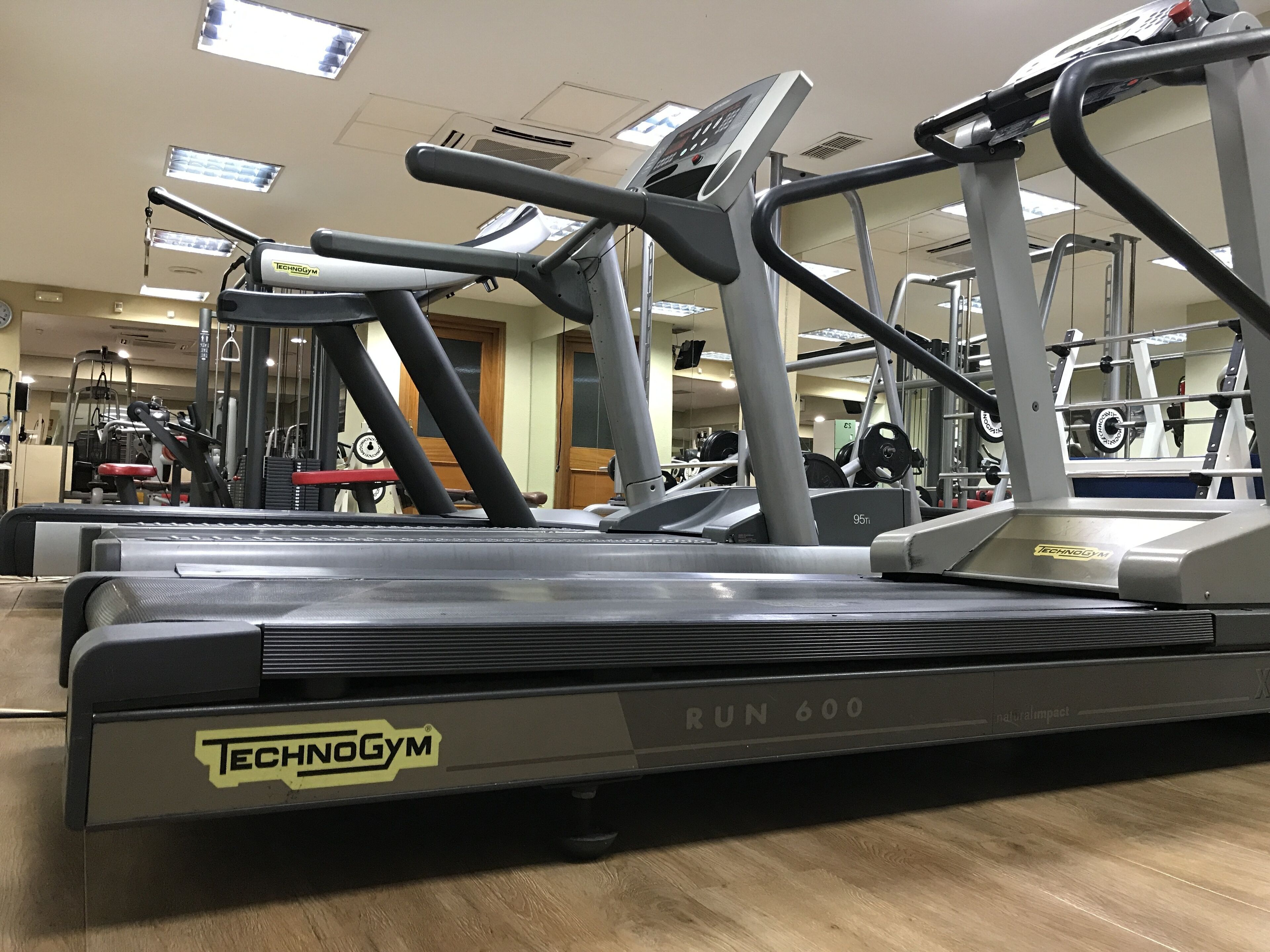 Un gimnasio con cintas de correr, máquinas de pesas y un muro de espejos.