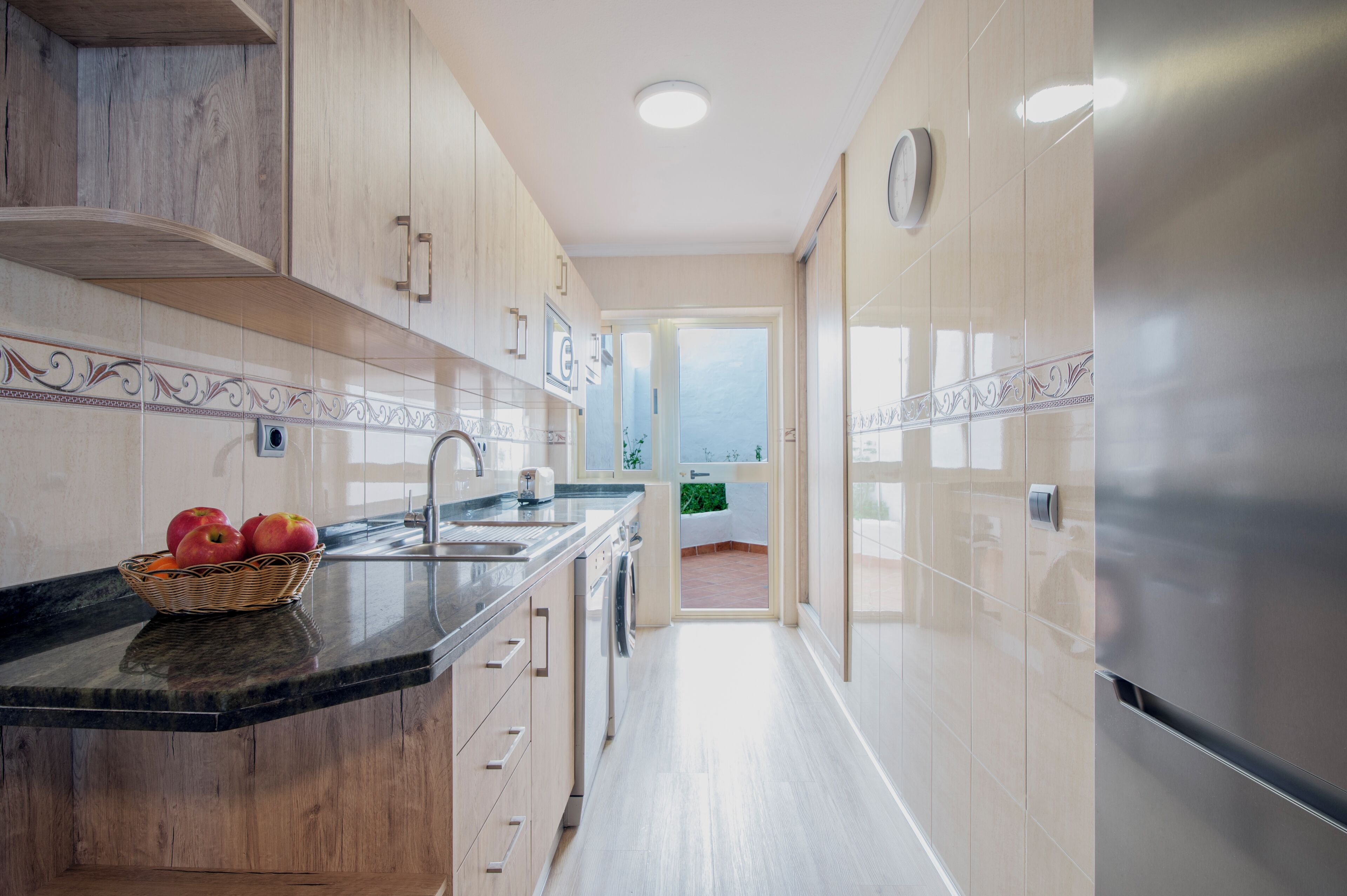 Une cuisine moderne avec des meubles en bois, un réfrigérateur en acier inoxydable et un plan de travail agrémenté d’un panier de fruits.