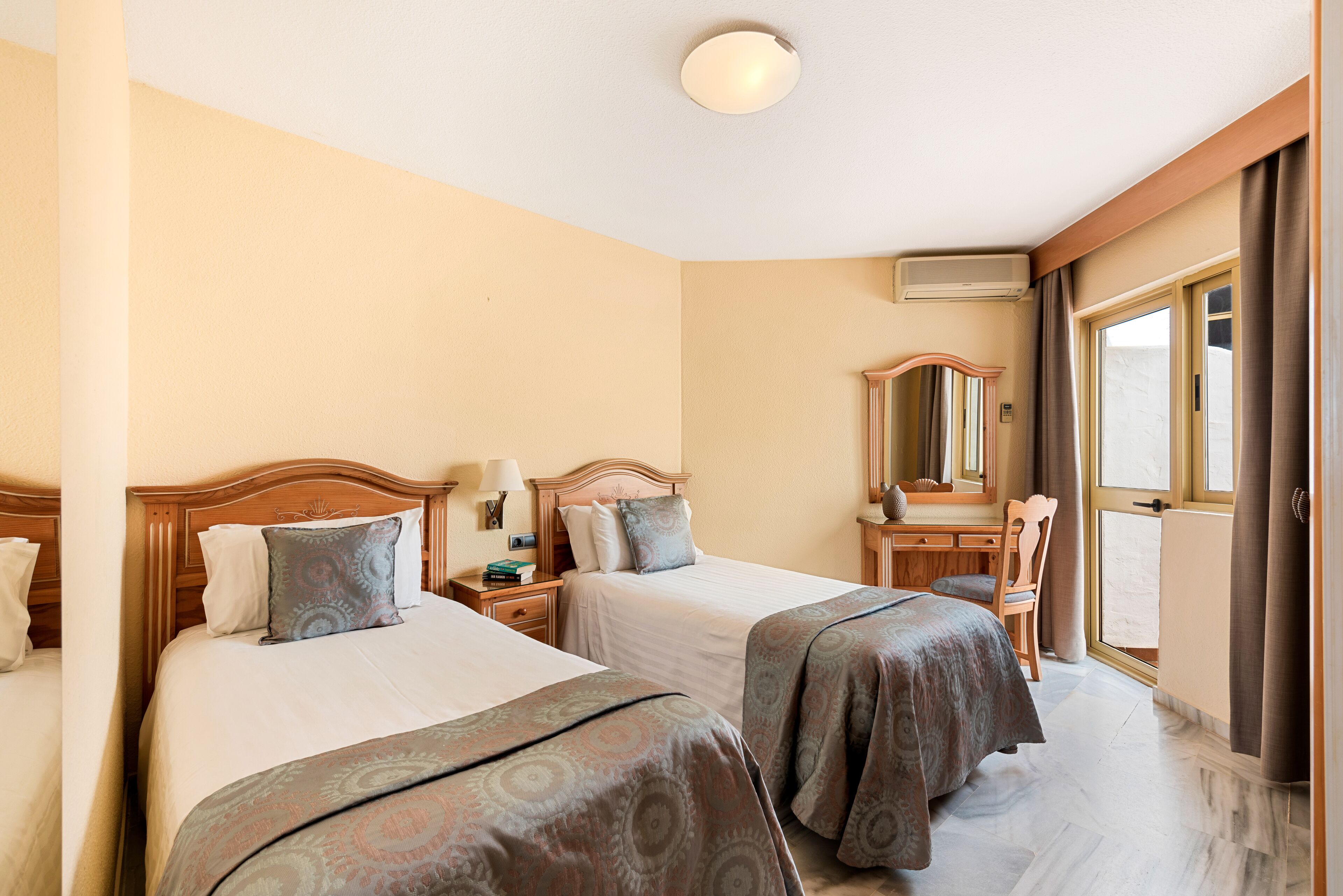 Una habitación de hotel con dos camas, un aparador, un espejo y una ventana con cortinas.