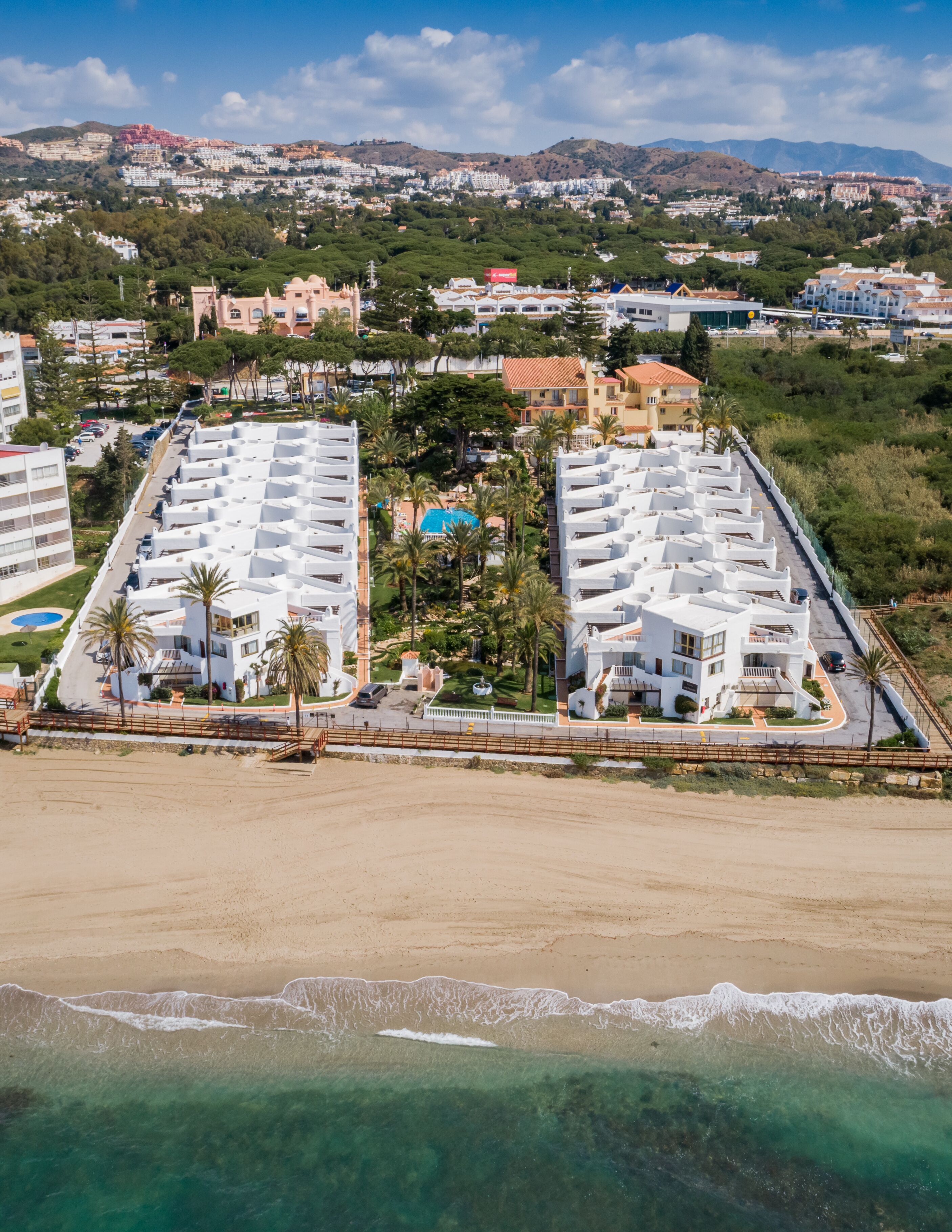 Um hotel costeiro com vários edifícios brancos, uma praia de areia e uma vista desimpedida do oceano.
