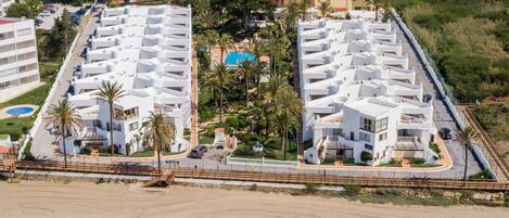 Um hotel costeiro com vários edifícios brancos, uma praia de areia e uma vista desimpedida do oceano.