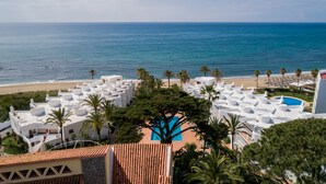 A resort with a pool surrounded by palm trees, overlooking a beach and the ocean.