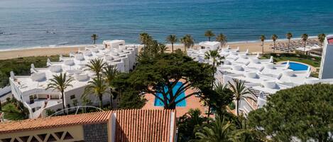 A resort with a pool surrounded by palm trees, overlooking a beach and the ocean.