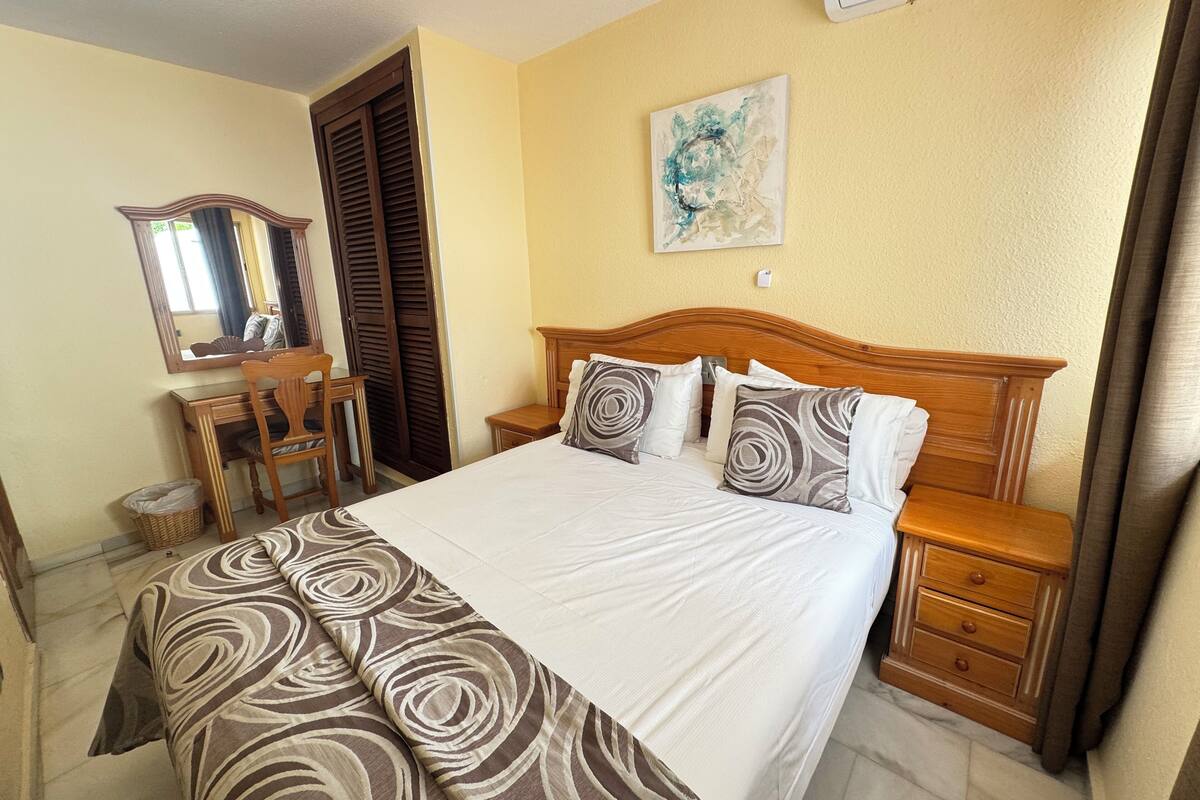 A neatly arranged bedroom with a bed, bedside tables, a dresser, a chair, and a mirror.