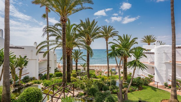 A resort with palm trees, a small pond, and a view of the ocean.