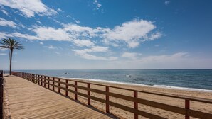 A wooden boardwalk leading to a beach with a palm tree and a clear blue sky.
