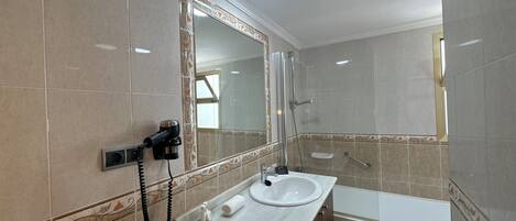 A bathroom with a sink, mirror, shower, and a hairdryer on the wall.