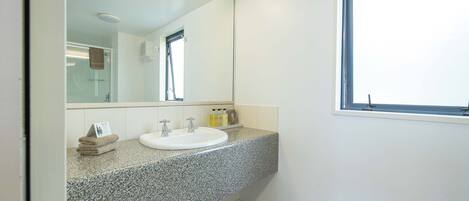 A bathroom with a granite countertop, a white sink, a large mirror, and a window.