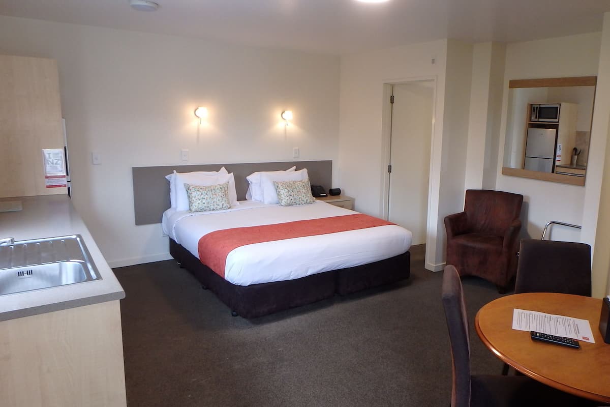 A hotel room with a bed, a desk, a chair, a microwave, a refrigerator, and a bathroom.