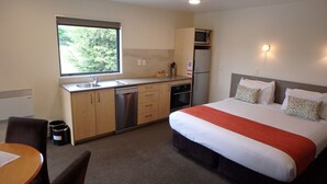 A compact hotel room with a kitchenette, a bed with a red blanket, and a view of greenery through the window. - Bella Vista Queenstown (Queenstown)