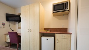 A compact room with a bed, a desk, a chair, a small refrigerator, a microwave, and a TV mounted on the wall. - Bella Vista Queenstown (Queenstown)