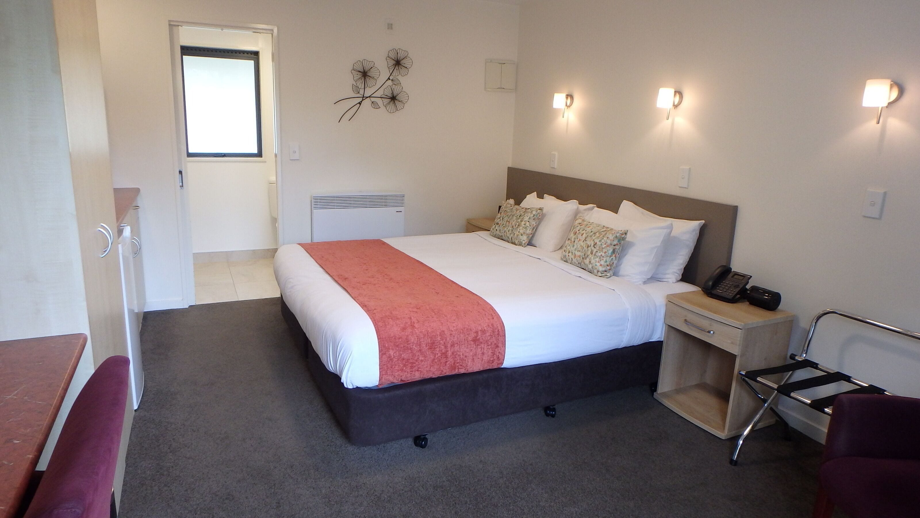 A hotel room with a bed, bedside table, chair, and a desk with a chair.