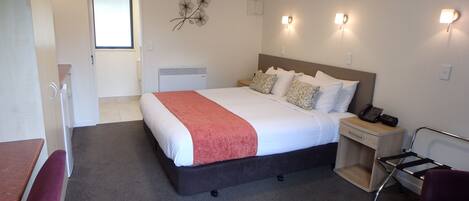 A hotel room with a bed, bedside table, chair, and a desk with a chair.
