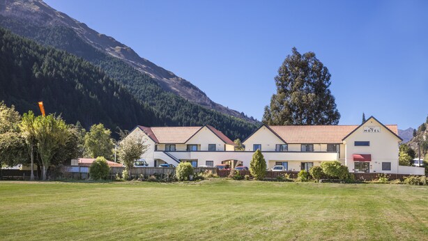 A motel with a red-tiled roof, surrounded by a grassy field and a mountain backdrop. - Bella Vista Queenstown (Queenstown)