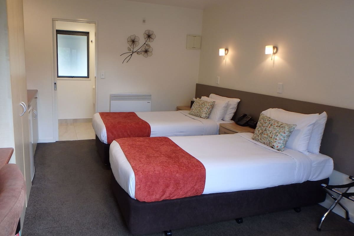 A hotel room with two beds, a desk, and a chair. There is a door leading to another room.