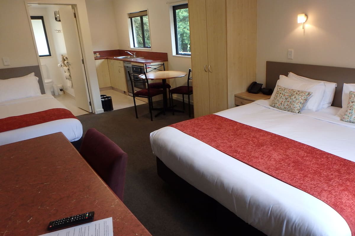 A hotel room with a large bed, two smaller beds, a desk with a chair, and a window.