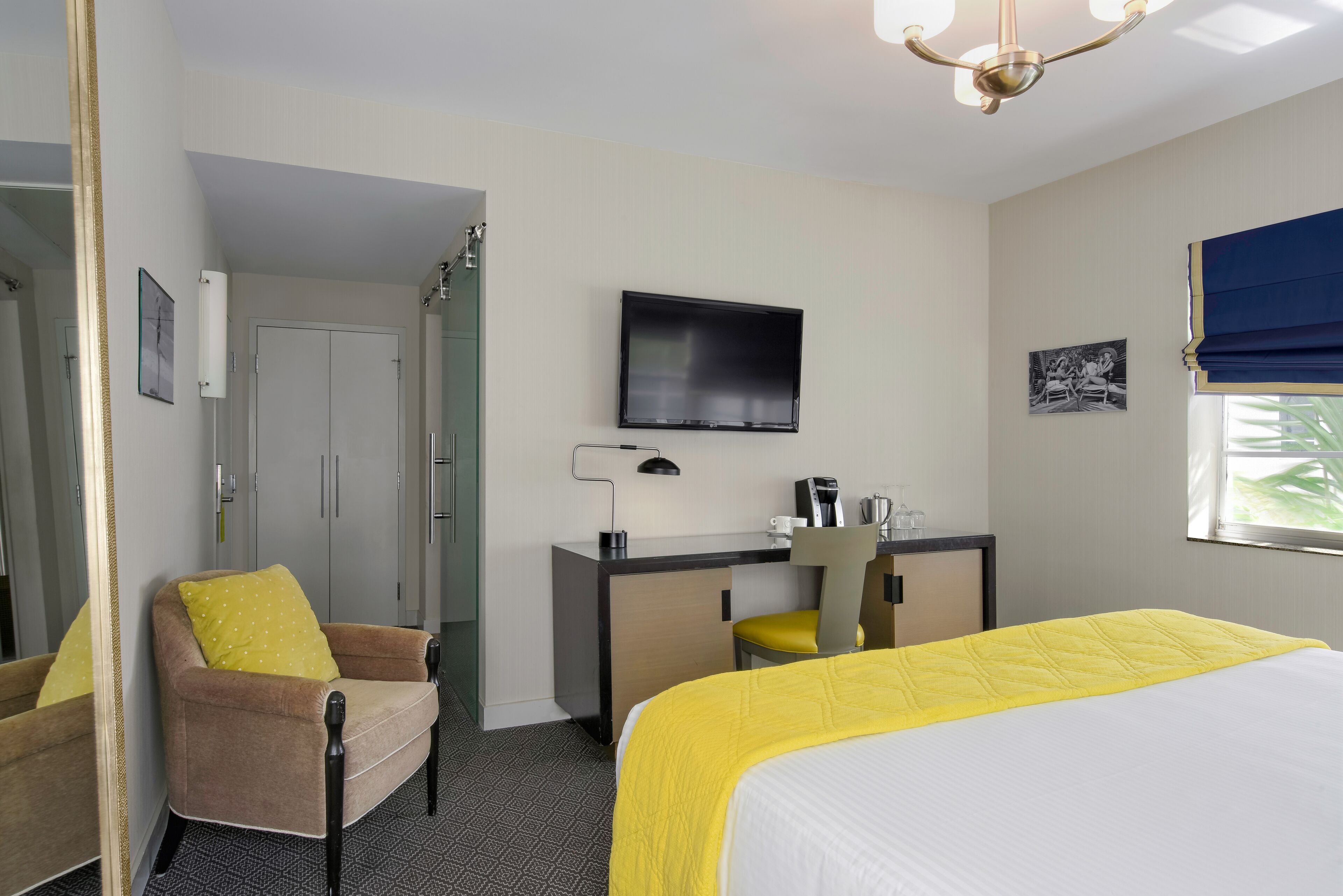 Una habitación de hotel con cama, escritorio, silla, televisor y espejo.