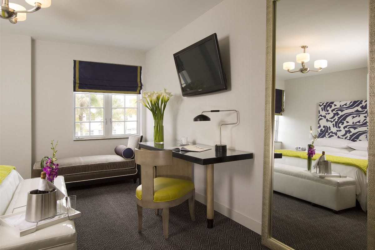 A hotel room with a desk, chair, television, bed, and a large mirror.
