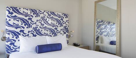 Une chambre d’hôtel avec un grand lit, une tête de lit à motifs bleus et blancs, une table de chevet avec un téléphone et un miroir au mur.