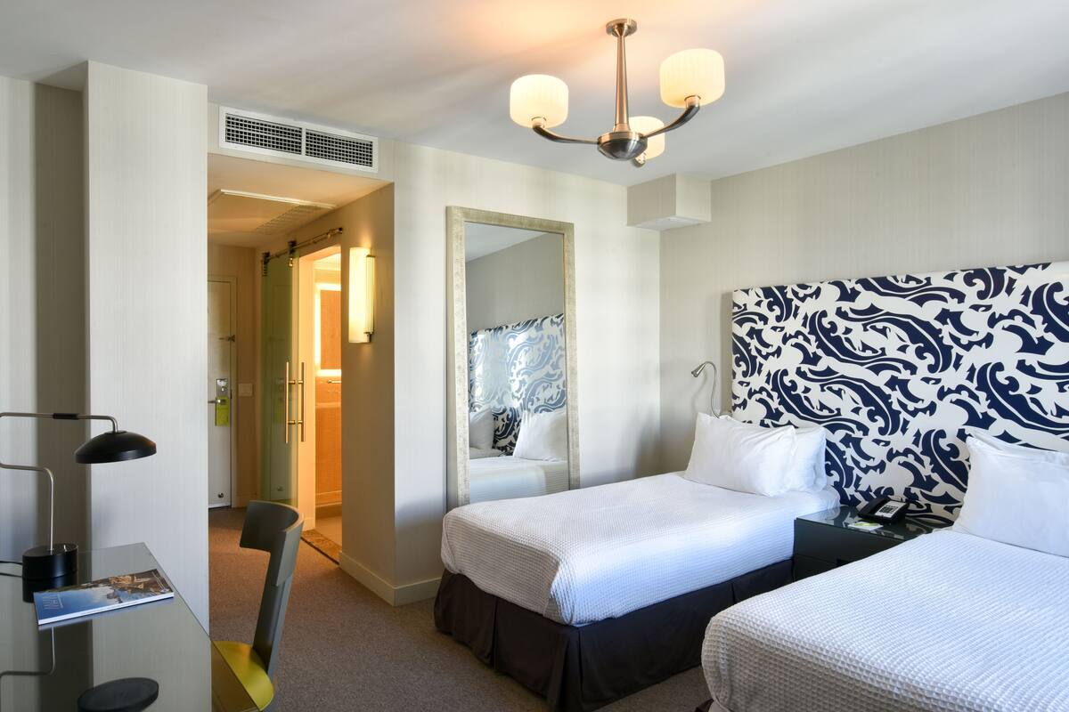 A hotel room with a bed, bedside table, lamp, chair, and a mirror.