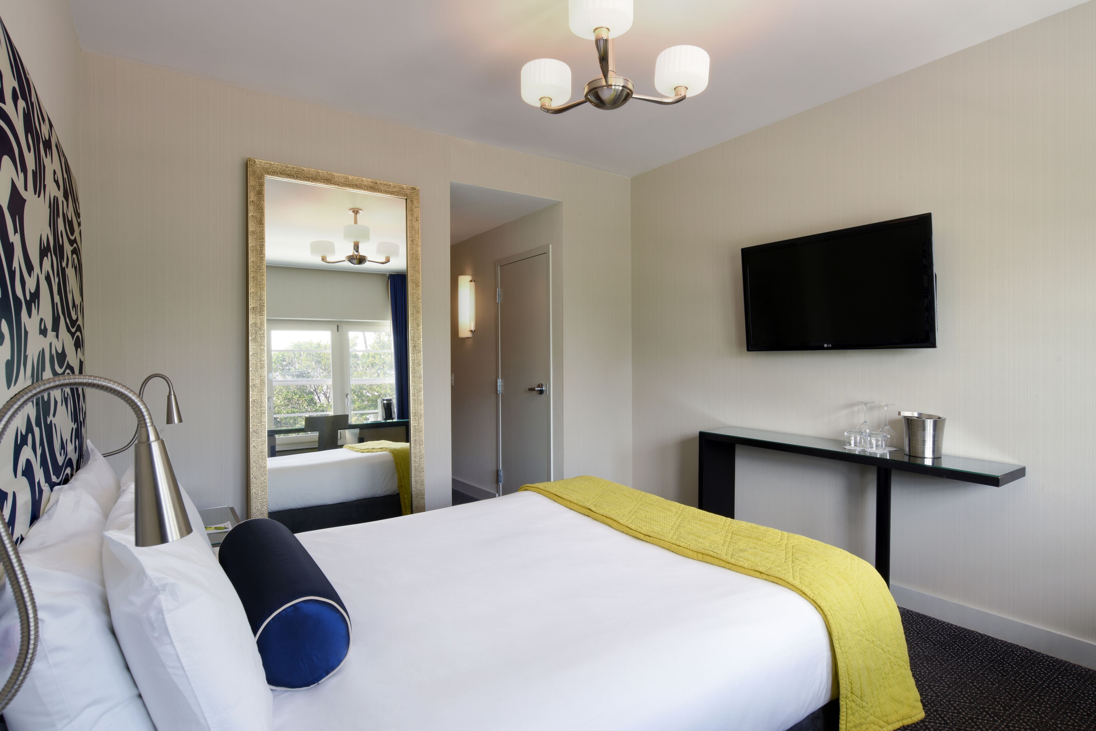 Una habitación de hotel con cama, mesita de noche, televisor y espejo.