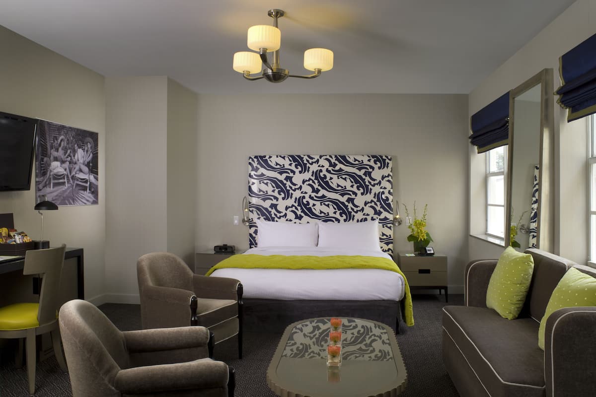 A hotel room with a bed, two armchairs, a sofa, a small table, a TV, and a patterned headboard.