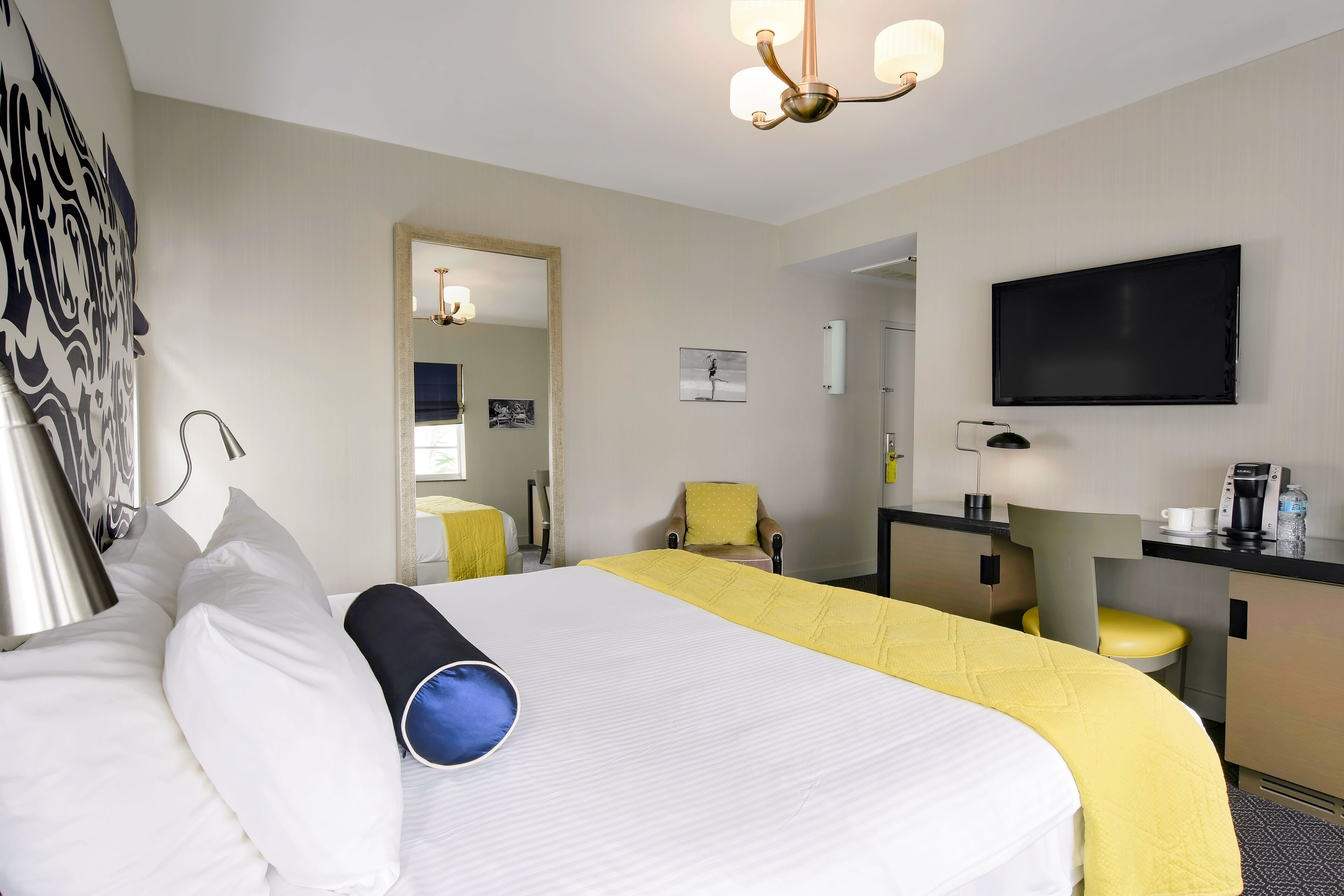 A hotel room with a bed, a desk, a chair, a television, and a mirror.