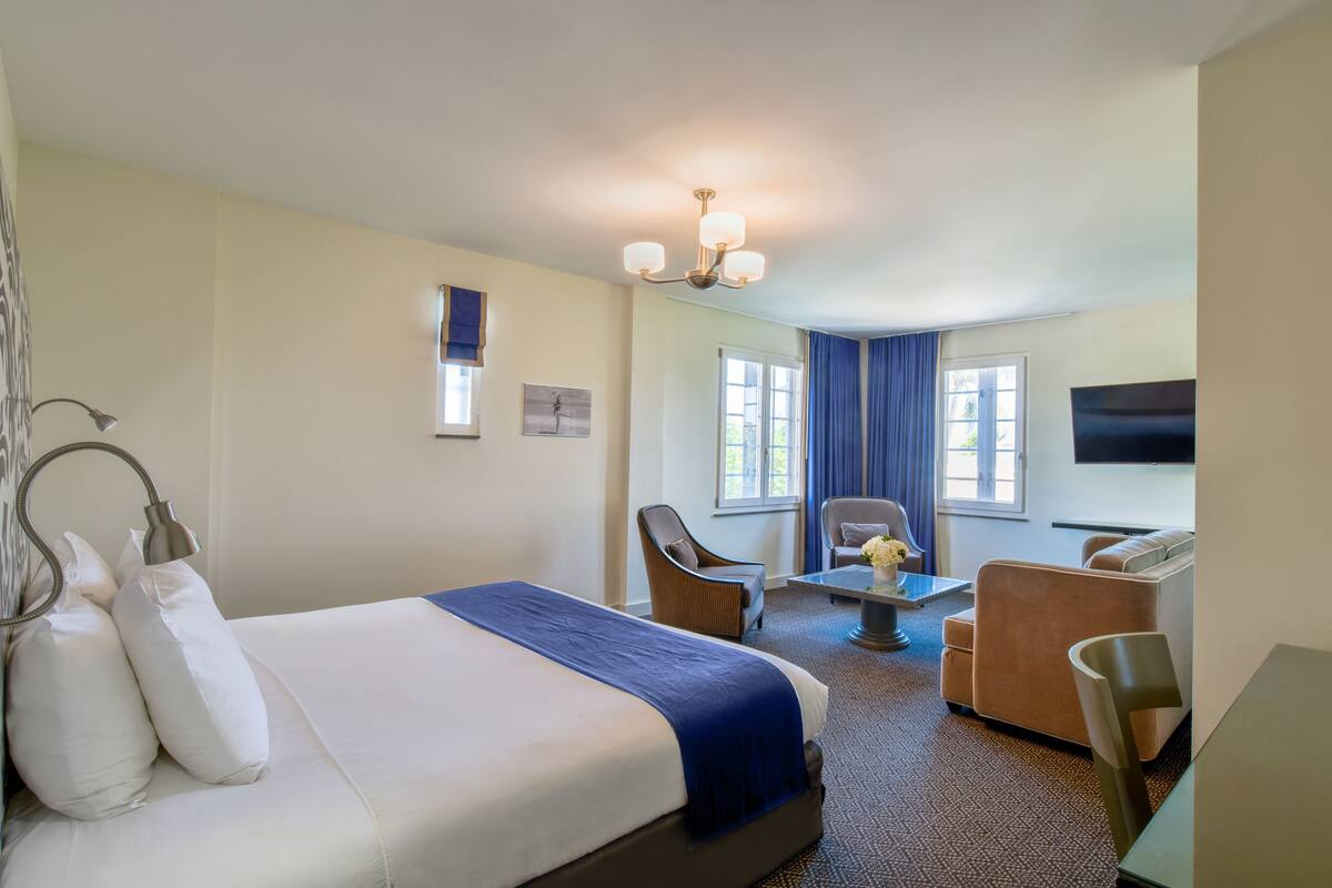 A hotel room with a large bed, a chair, a sofa, a small table, and a TV.