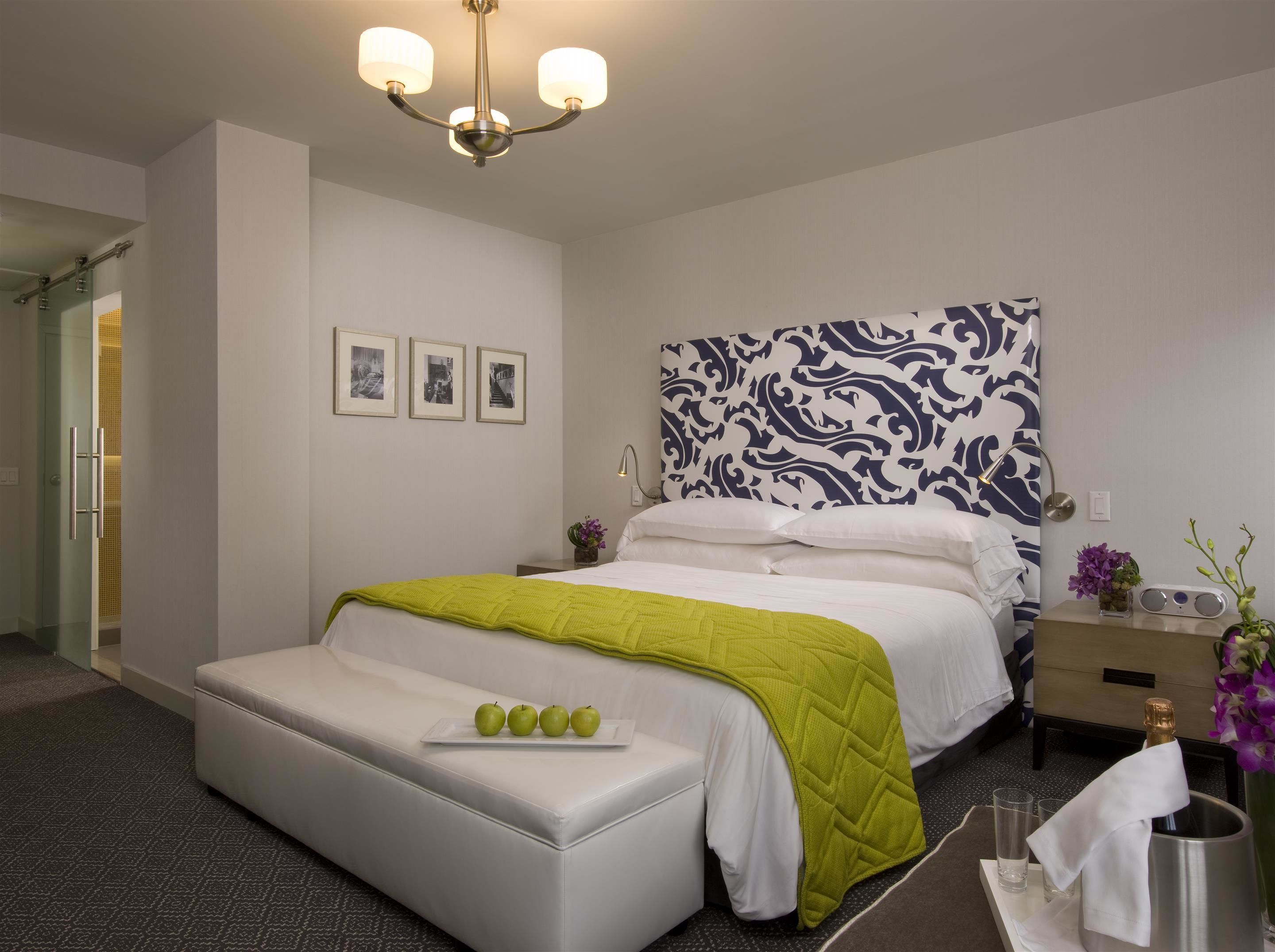 A hotel room with a bed, a bedside table with a lamp, a nightstand with a vase of flowers, and a wall with three framed pictures.