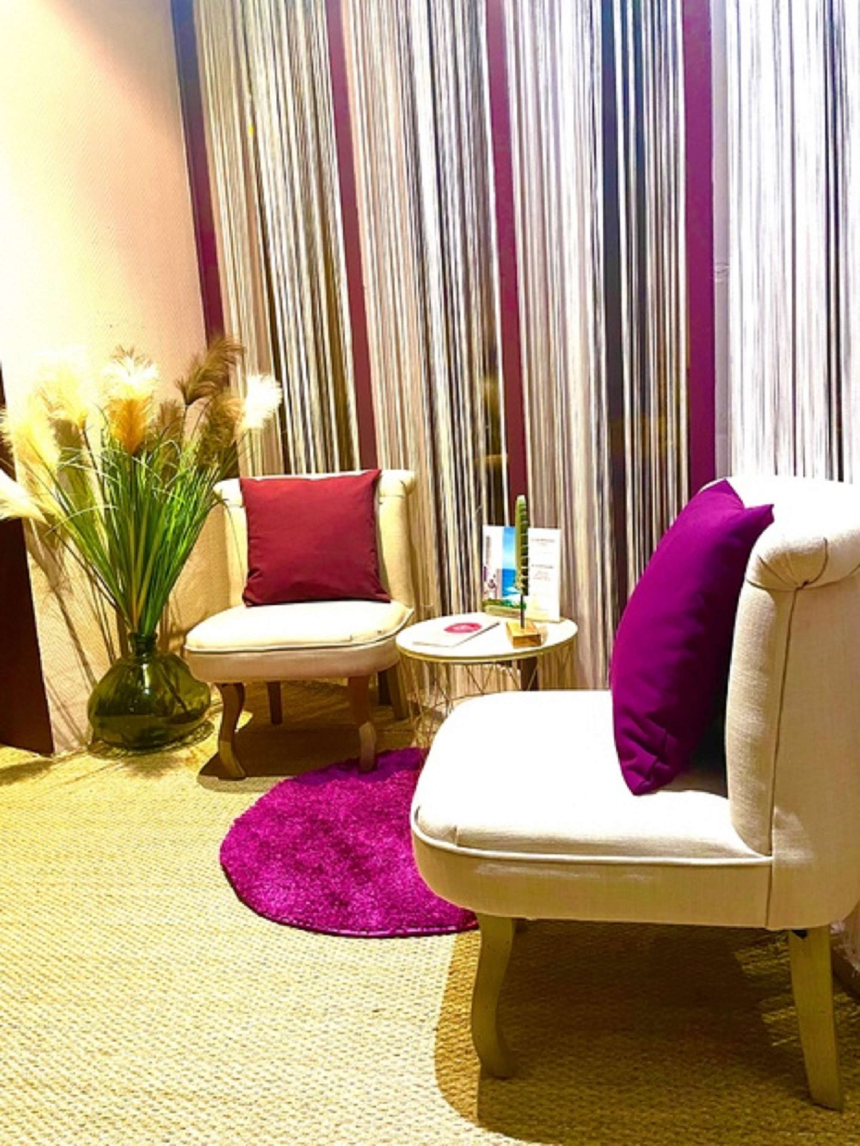 Una habitación con un sofá blanco, un cojín rojo, una mesita redonda y un jarrón con plantas secas.