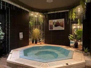 A hot tub with a tiled deck, surrounded by dark walls and potted plants.