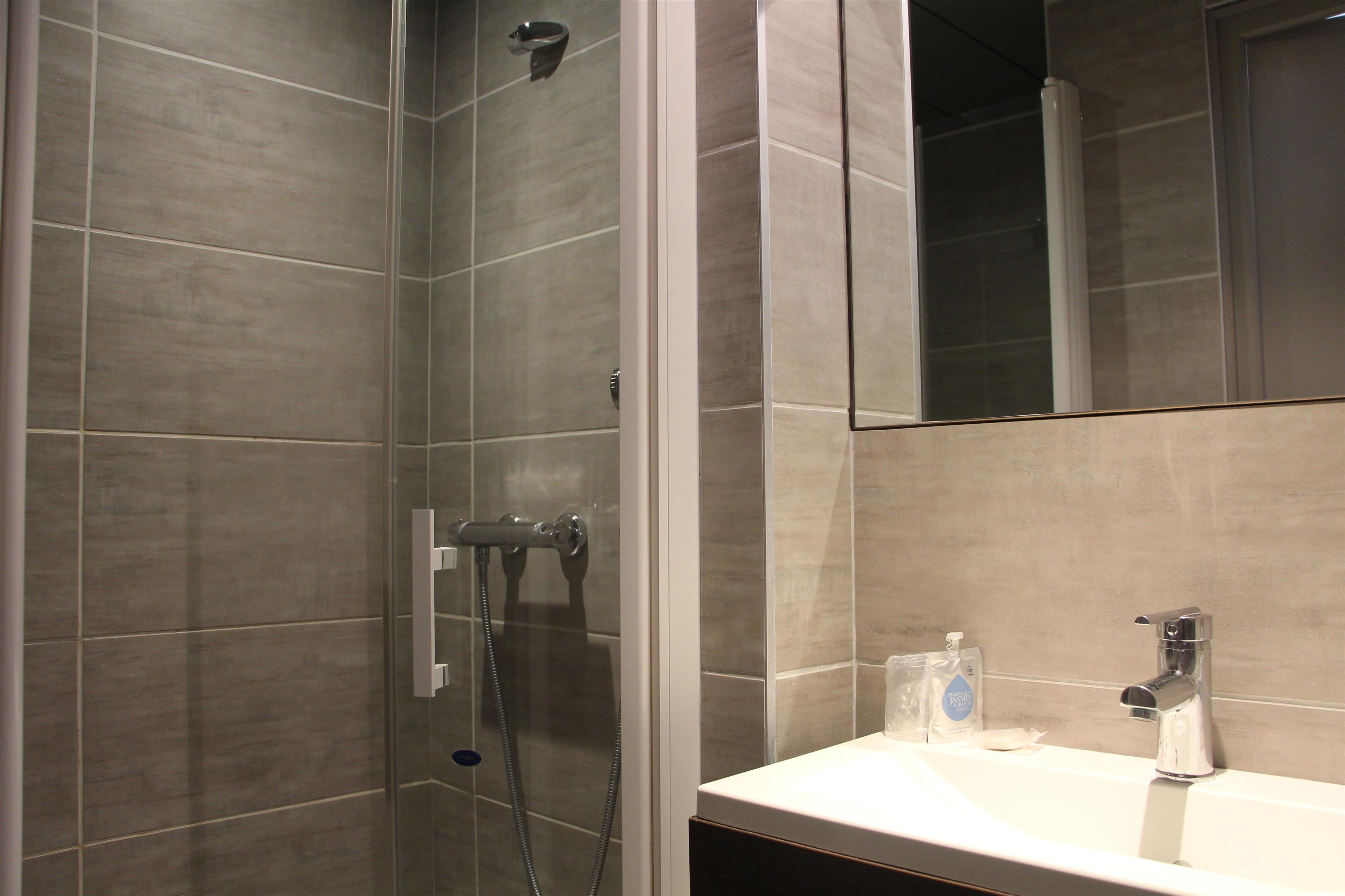 A modern bathroom with a glass-enclosed shower, a sink with a mirror, and a bottle of hand soap on the counter.