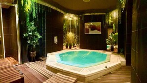 A hot tub surrounded by dark walls and wooden flooring, with potted plants and a wooden bench. - Hotel Kyriad Vichy Spa Cinq Mondes (Vichy)