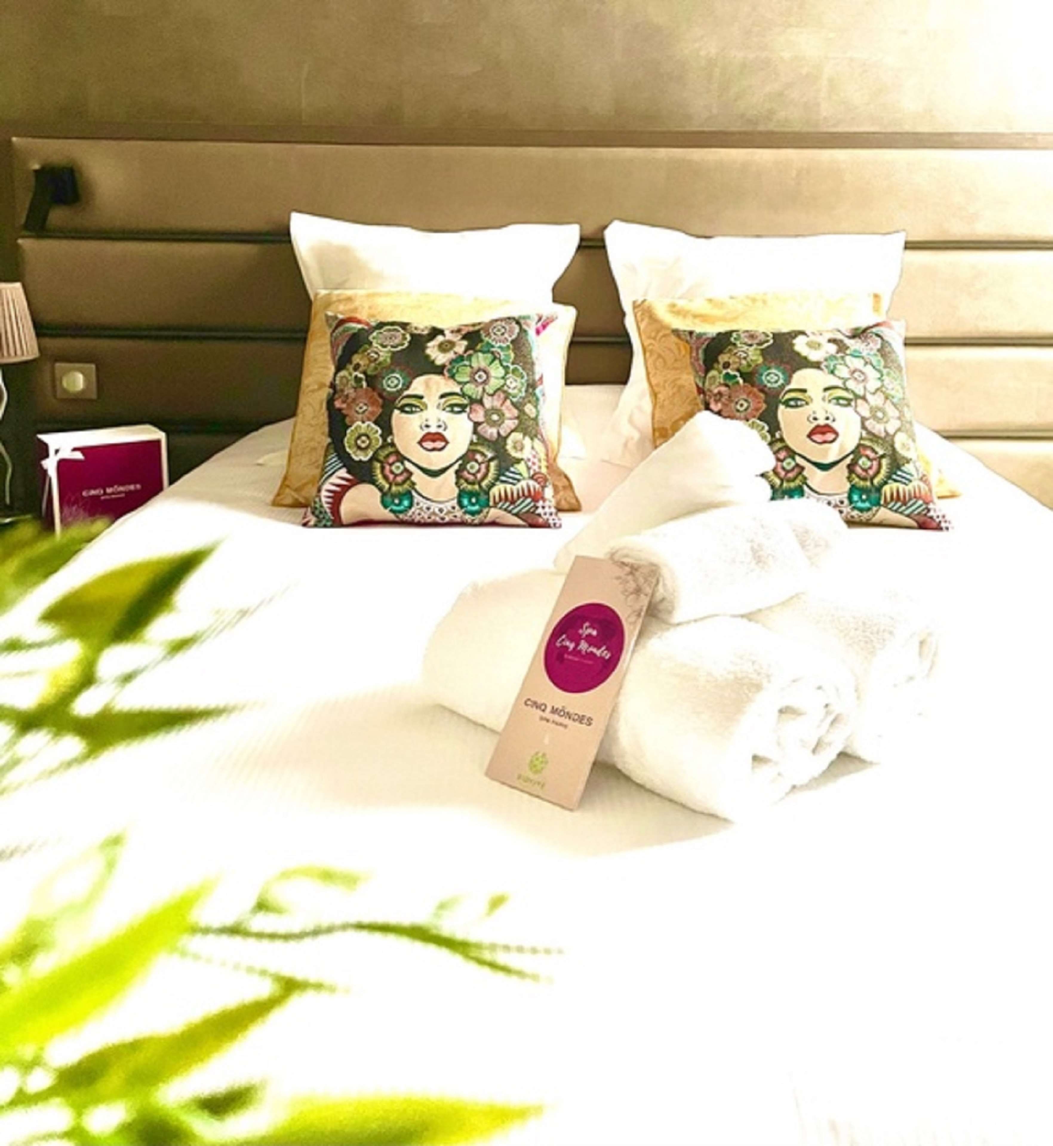 Un letto con due cuscini decorativi, un asciugamano bianco arrotolato e una piccola scatola con un'etichetta.