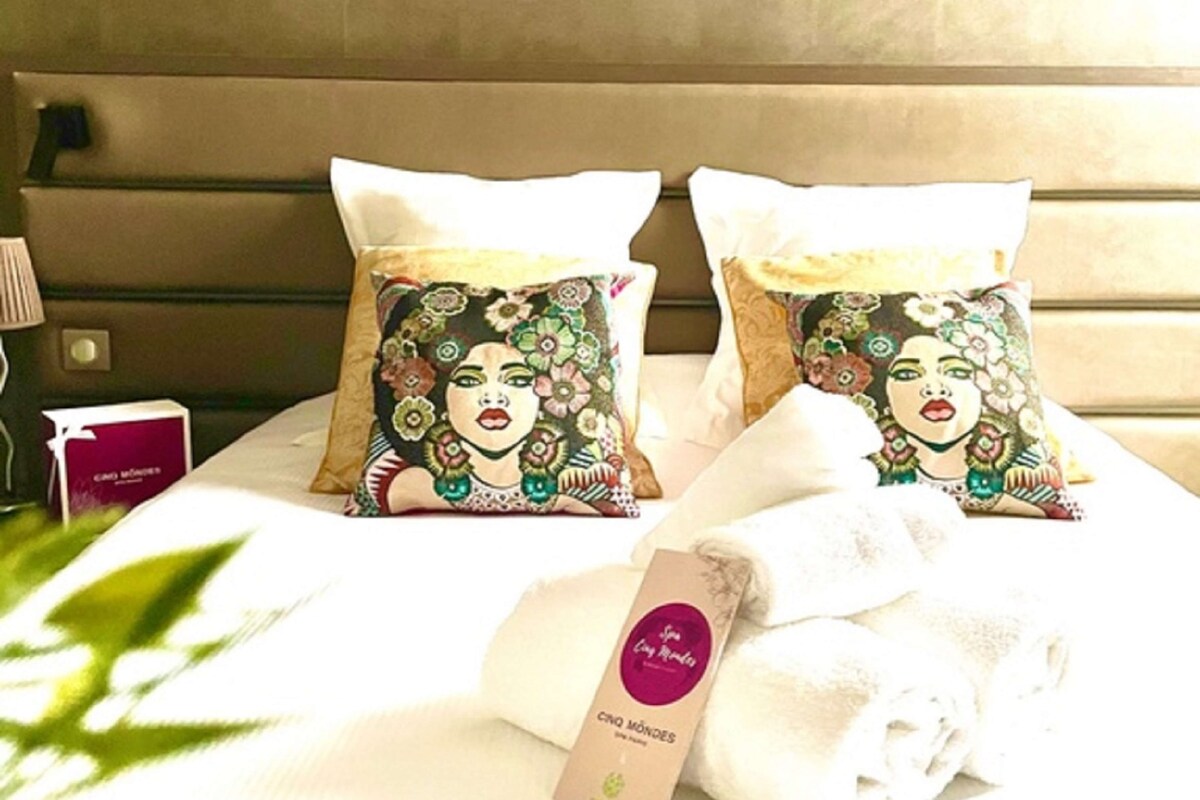 Una cama con dos almohadones decorativos, una toalla blanca enrollada y una tarjeta sobre la cama.