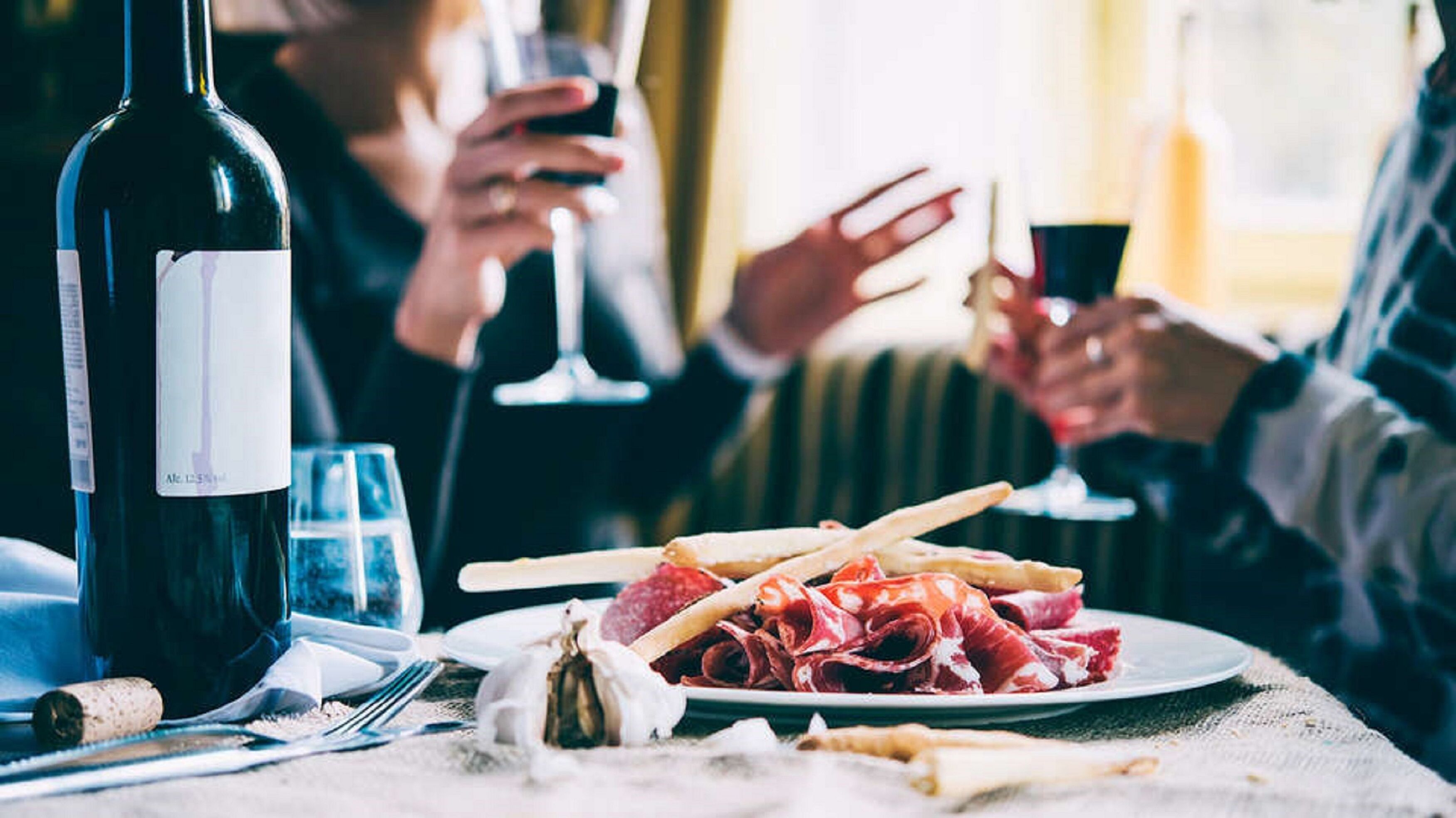 Une table à manger avec une bouteille de vin, des verres et une assiette de nourriture.