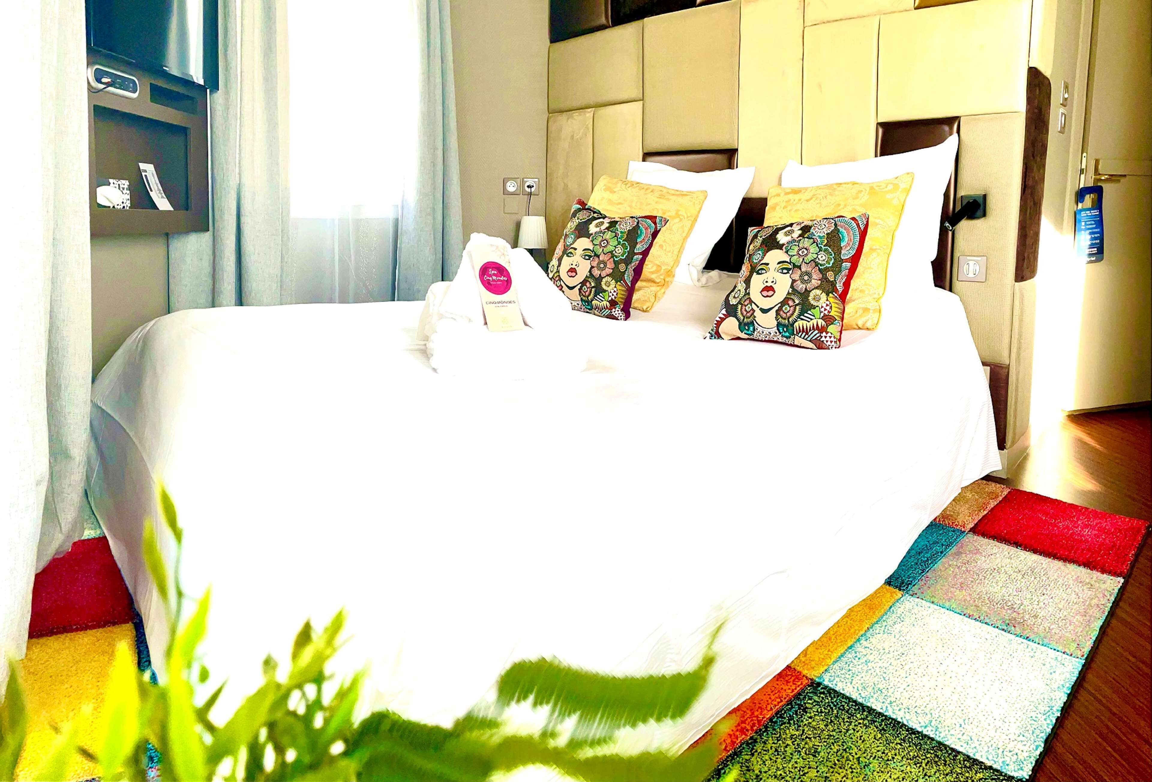 A neatly made bed with floral pillows, a bedside table with a lamp, and a television above it.