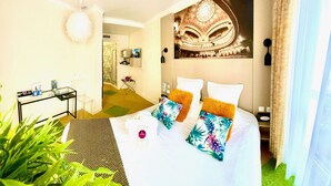 A hotel room with a bed, a small table with a coffee maker, a plant, and a wall with a theater mural. - Hotel Kyriad Vichy Spa Cinq Mondes (Vichy)
